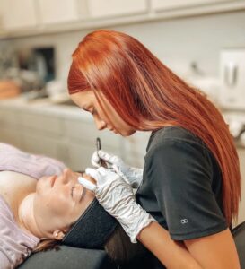 A woman is giving a man an eyebrow tattoo.