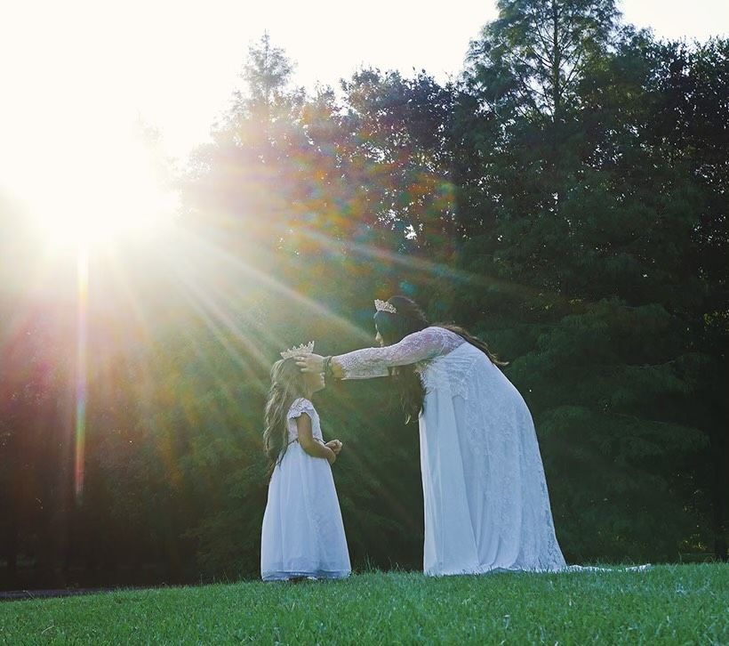 A woman and child in white dress on grass.